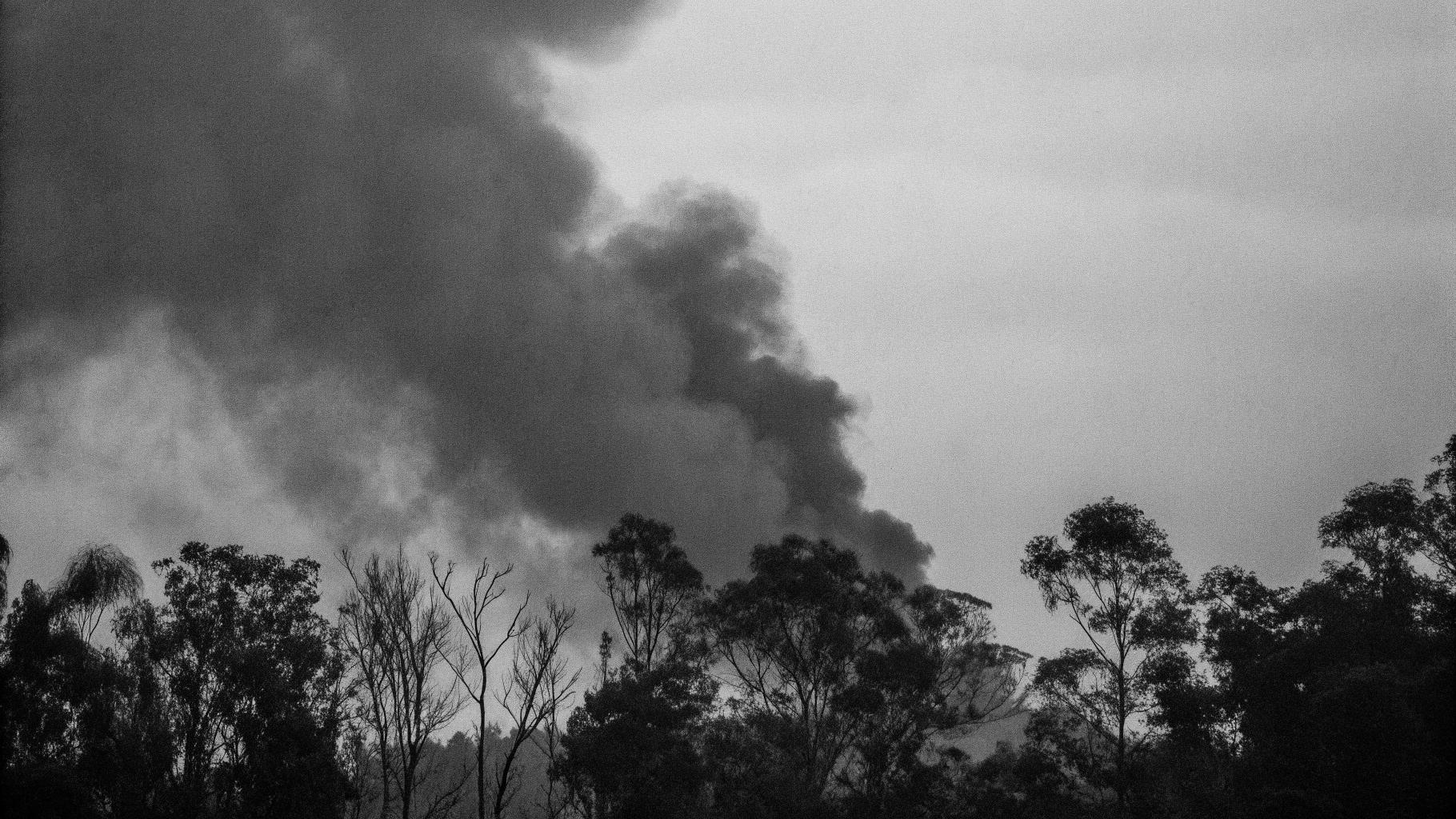 Illustration abstraite d'un incendie de forêt en silhouette, avec des flammes orangées et des nuées de fumée grise, dans un style presse sérieuse, format paysage 3:2