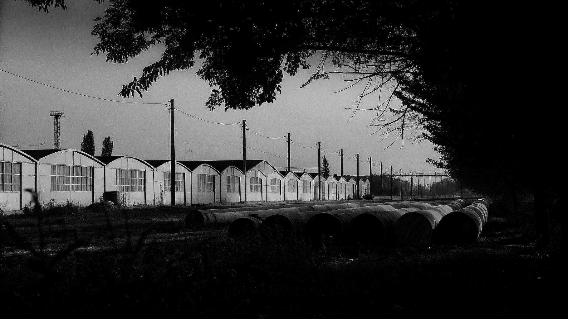 Zone industrielle textile à Prato avec entrepôts anonymes et atmosphère de tension économique