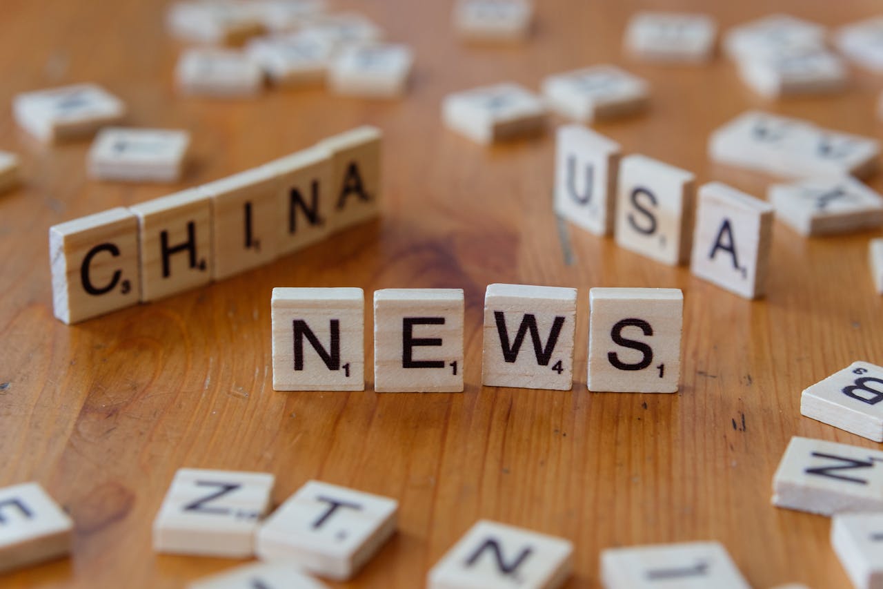 team-03 Wooden Scrabble tiles spelling 'NEWS' with 'CHINA' and 'USA' on a wooden surface.